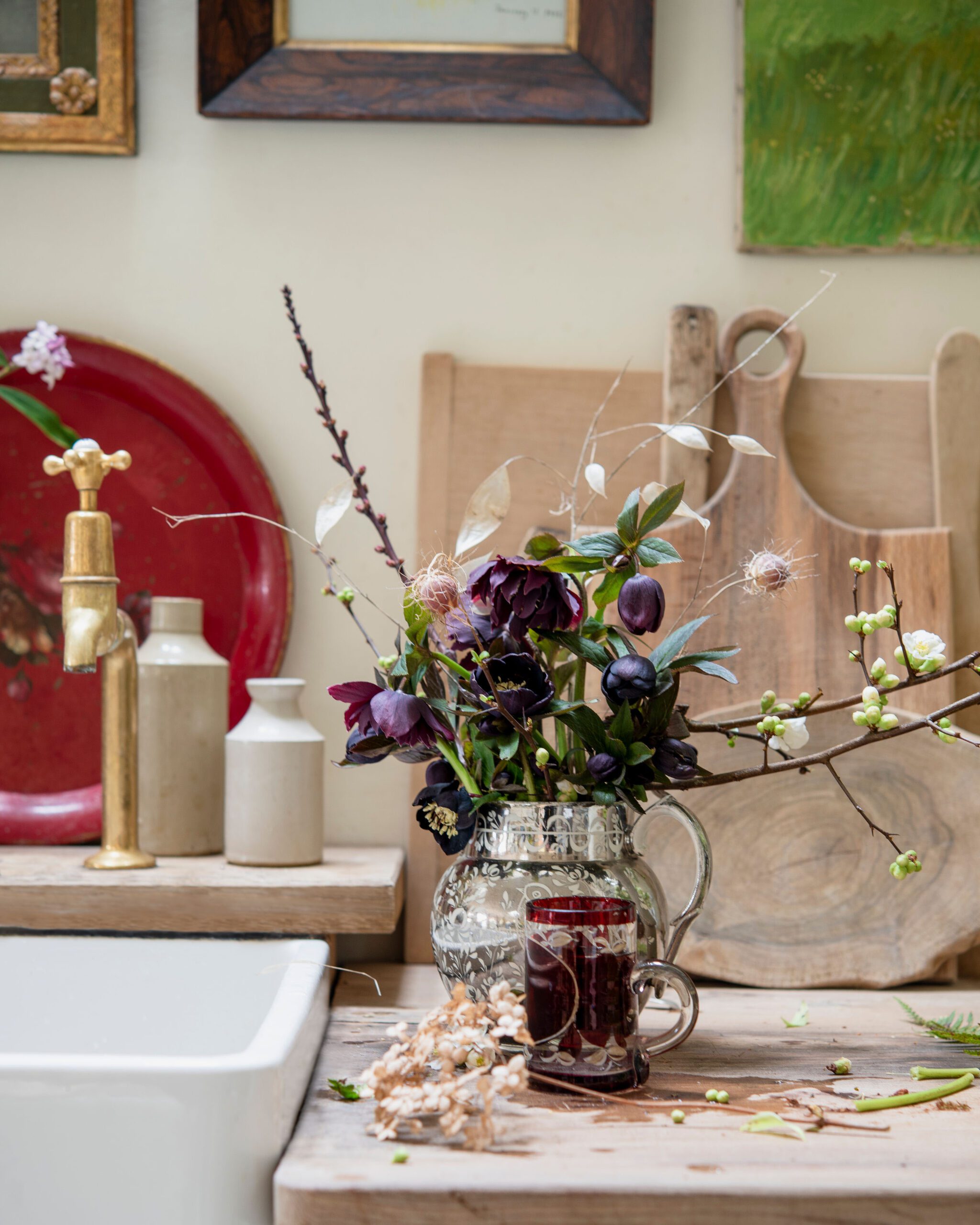 A vase of flowers on a wooden board alongside a white, ceramic kitchen sink.